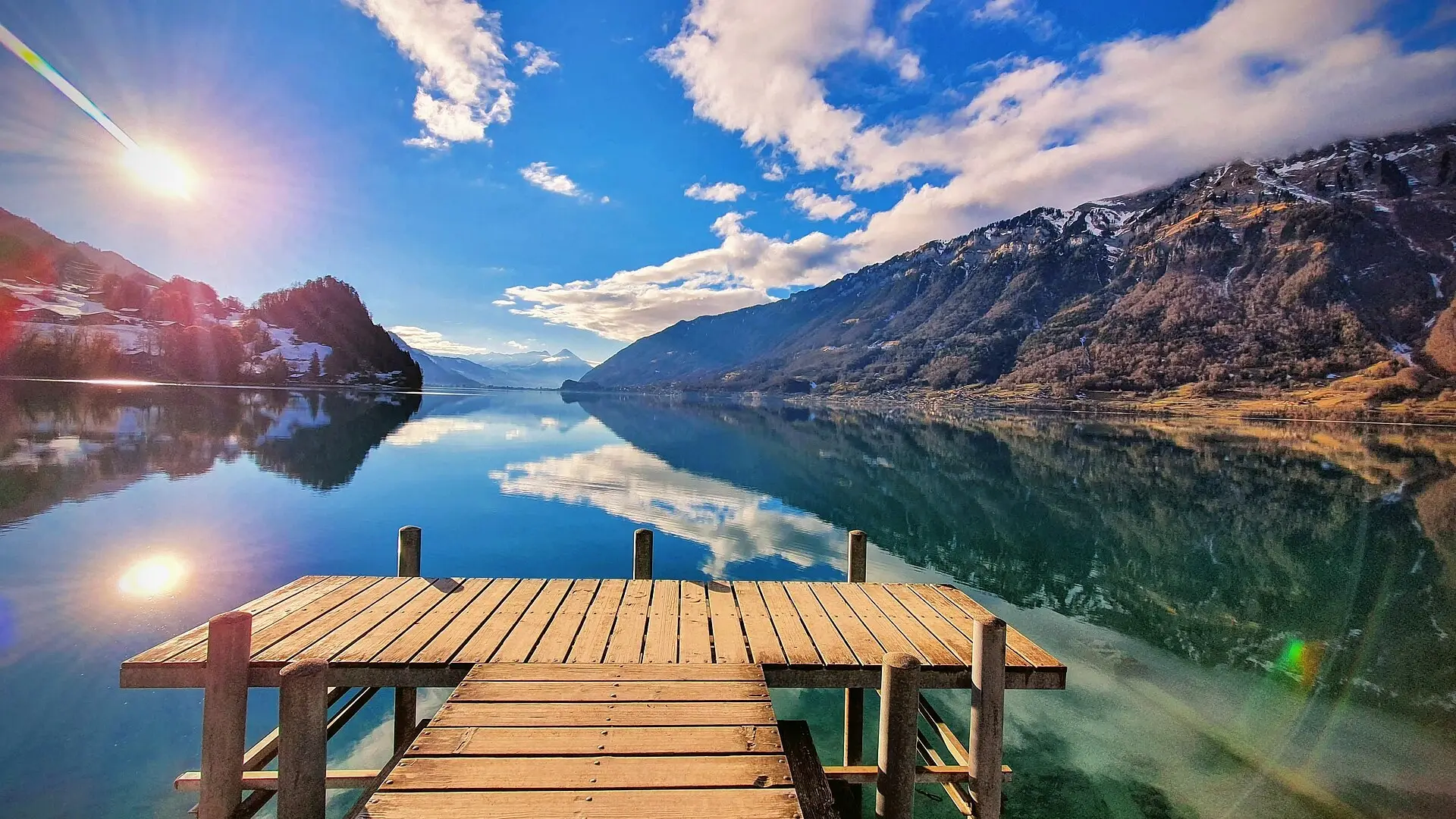 A man kneeling with a ring on a lakeside path in the Swiss Alps as his partner covers her mouth in surprise